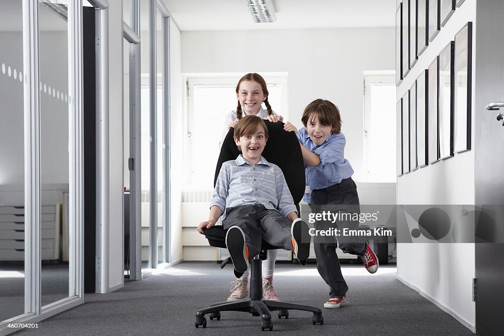 Three children playing in office corridor on office chair