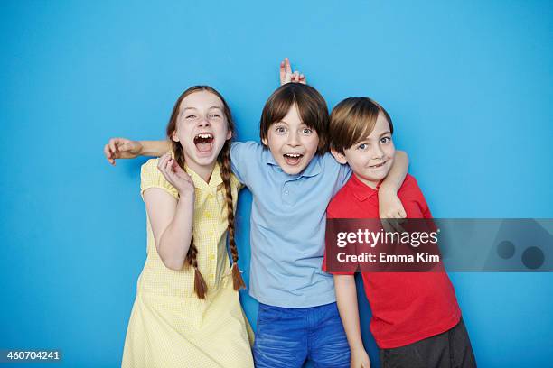 portrait of three children with arms around each other against blue background - children only laughing stock pictures, royalty-free photos & images