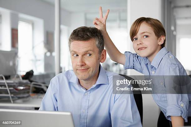 father using laptop, son making peace sign behind his head - rolwisseling stockfoto's en -beelden