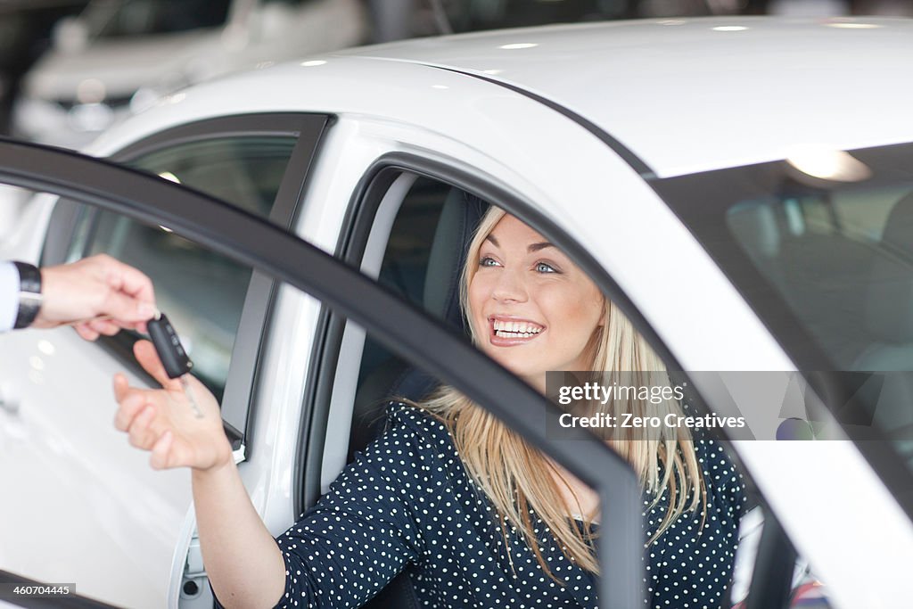 Young woman sitting in new car with key in showroom
