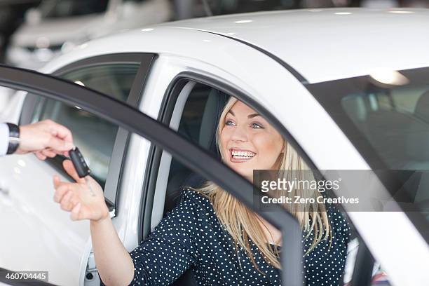young woman sitting in new car with key in showroom - happy car customer stock-fotos und bilder