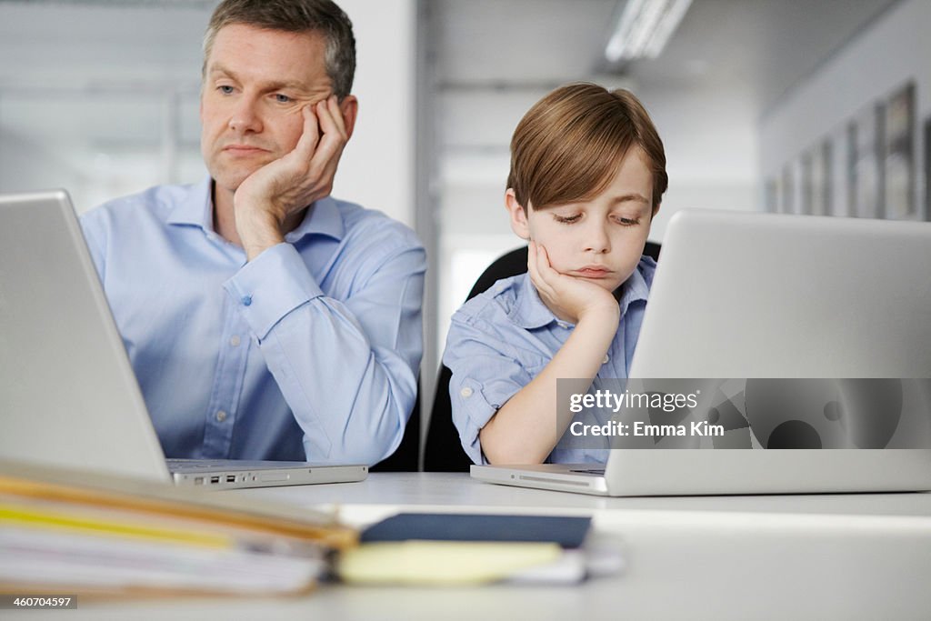 Father and son using laptops looking bored