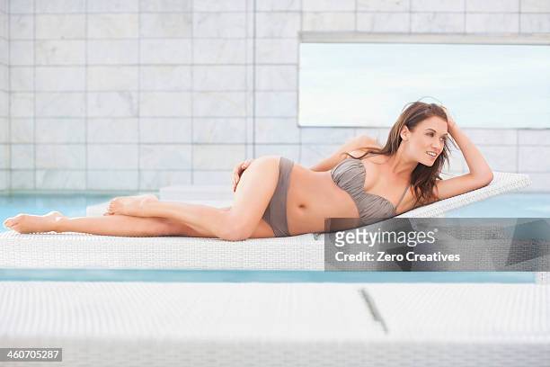mid adult woman in bikini lying on pool sunbed - einzelne frau über 30 stock-fotos und bilder