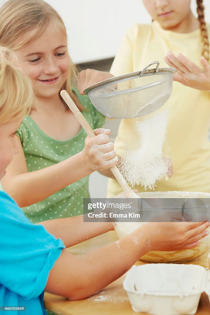 Children baking, sieving flour into mixing bowl