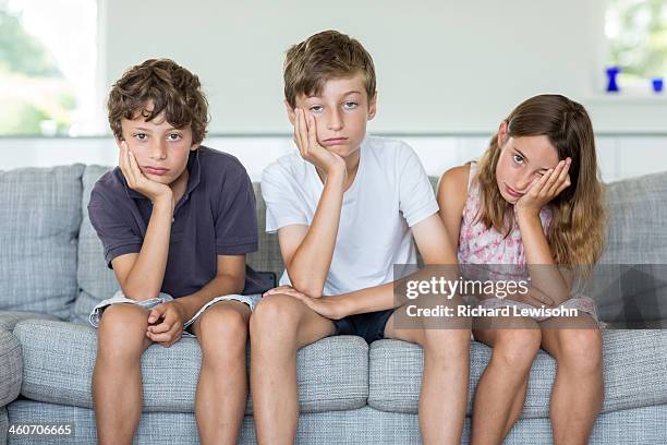 brothers and sister on sofa looking bored - angry boy stockfoto's en -beelden