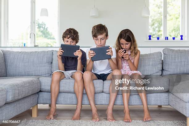 brothers and sister on sofa with digital tablets and mobile - gaming mobile stock pictures, royalty-free photos & images