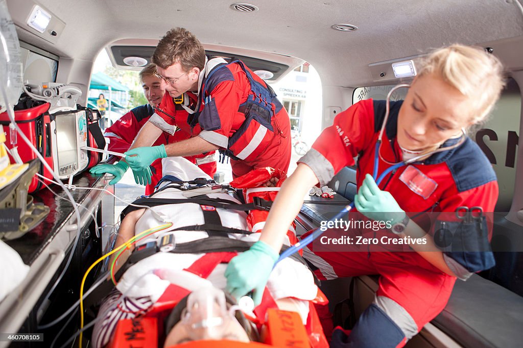 Paramedics using stethoscope on patient in ambulance
