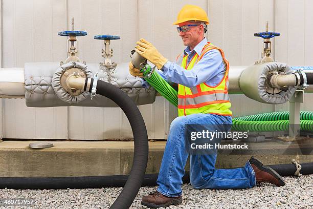 engineer at electric power plant examining connection hose near water storage tank - industrial hose stockfoto's en -beelden