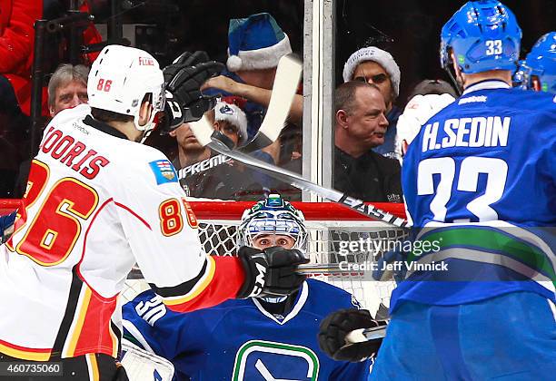 Ryan Miller of the Vancouver Canucks eyes the puck between the sticks as Josh Jooris of the Calgary Flames and Henrik Sedin of the Canucks watch...