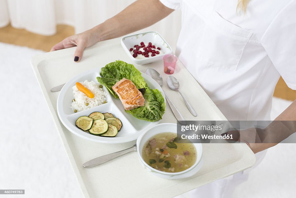 Germany, Young woman holding patient tray with main meal, close up