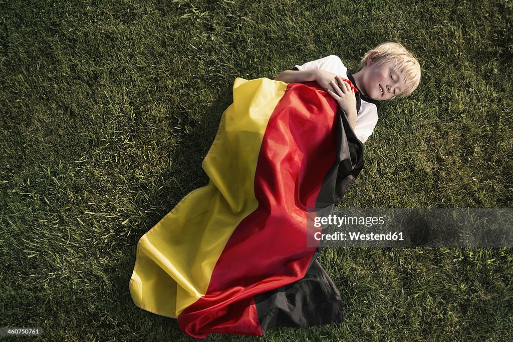 Germany, Cologne, Young football fan sleeping wrapped in German Flag
