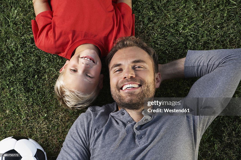 Germany, Cologne, Father and son lying in meadow