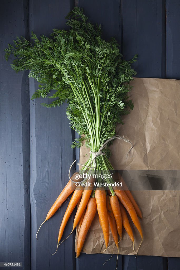 Carrots with brown paper on wooden table, close up