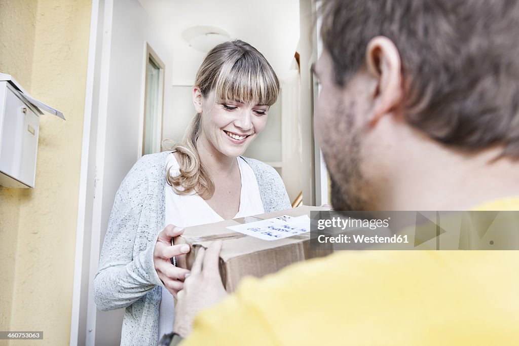 Germany, North Rhine Westphalia, Cologne, Young woman taking pizza box from delivery man, smiling