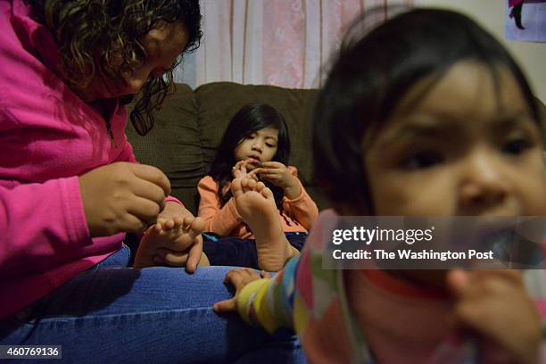 Marilu Morales paints the toenails of her daughter, Heidi Jocelyn Flores Morales as her one-year-old daughter, Mia Flores Morales, chews an ink pen...