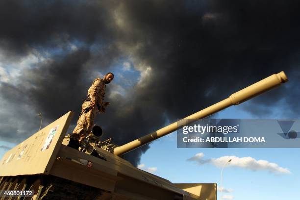 Member of the Libyan army stands on a tank as heavy black smoke rises from the city's port in the background after a fire broke out at a car tyre...