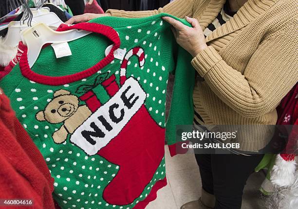 Irene Lopez, manager of Frugalista second hand store, shows off the store's supply of "ugly" Christmas sweaters in Washington, DC, December 23, 2014....