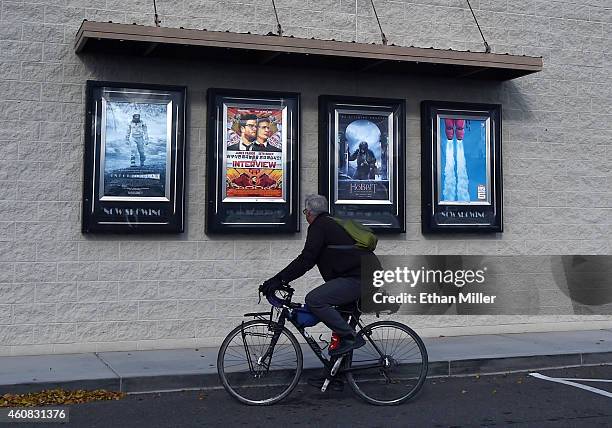 Man on a bicycle looks at movie posters, including one for "The Interview," outside the Megaplex Theatres - Stadium 6 as the Sony Pictures' film...