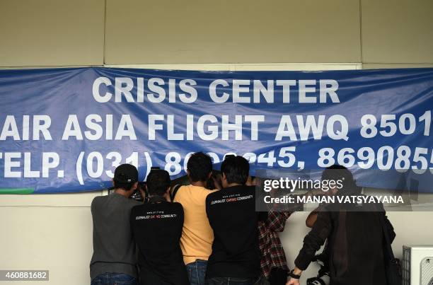 Media photographers try to take pictures of family members of passengers onboard missing Malaysian air carrier AirAsia flight QZ8501 as they sit...