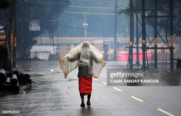 An Indian Sadhu uses a plastic sheet to shelter from rain as he walks along a street in Allahabad on January 1 on the occasion of New Year. AFP PHOTO...