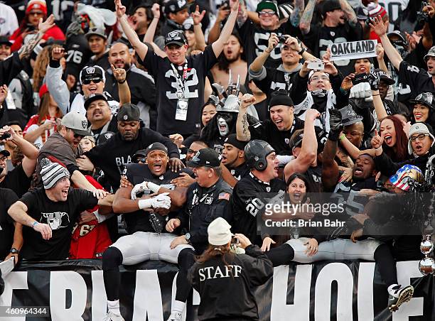 Wide receiver Brice Butler and linebacker Sio Moore of the Oakland Raiders jump into the arms of fans in the Black Hole after defeating the San...