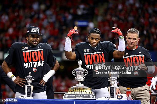 Darron Lee and Ezekiel Elliott and head coach Urban Meyer of the Ohio State Buckeyes celebrate with the trophy after defeating the Alabama Crimson...