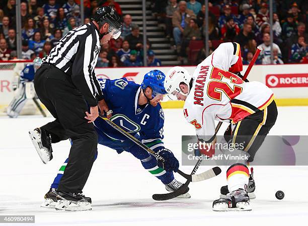 Linesman Jay Sharrers faces off the puck between Henrik Sedin of the Vancouver Canucks and Sean Monahan of the Calgary Flames during their NHL game...