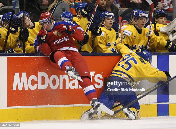 Russia's Ivan Barbashev lays a hit on Sweden's Axel Holmstrom in front of the Swedish bench. 2015 IIHF World Junior Championship hockey, 1st period...