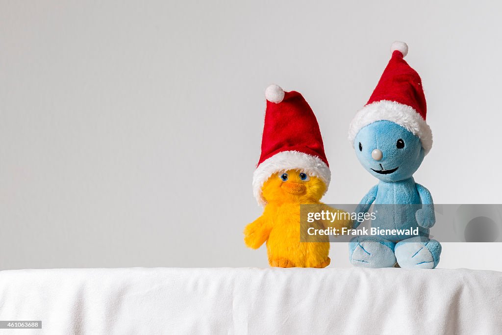 A light blue and a yellow cuddly toy, wearing Santa Claus...
