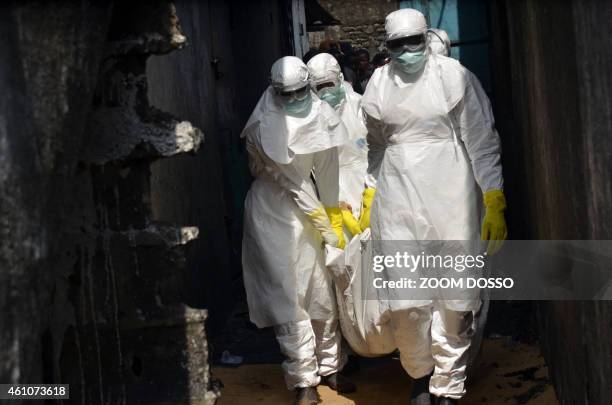 Red cross workers, wearing protective suits, carry the body of a person who died from Ebola during a burial with relatives of the victims of the...