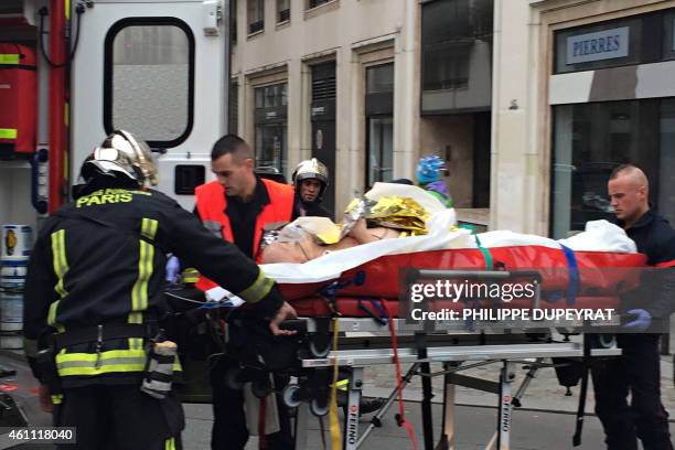 Firefighters carry an injured man on a stretcher in front of the offices of the French satirical newspaper Charlie Hebdo in Paris on January 7 after...