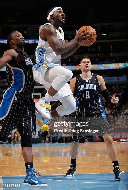 Ty Lawson of the Denver Nuggets lays up a shot between Ben Gordon and Nikola Vucevic of the Orlando Magic at Pepsi Center on January 7, 2015 in...