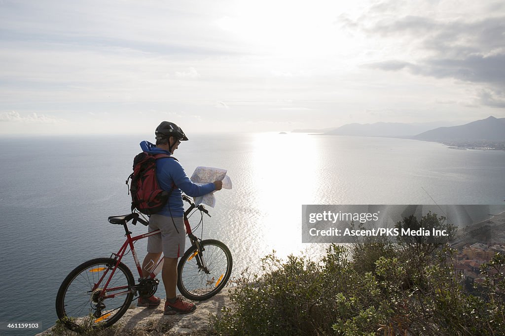 Mountain biker studeis map at cliff edge,sea below