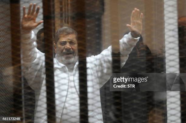 Egypt's deposed Islamist president Mohamed Morsi waves from inside the defendants cage during his trial at the police academy in Cairo on January 8,...