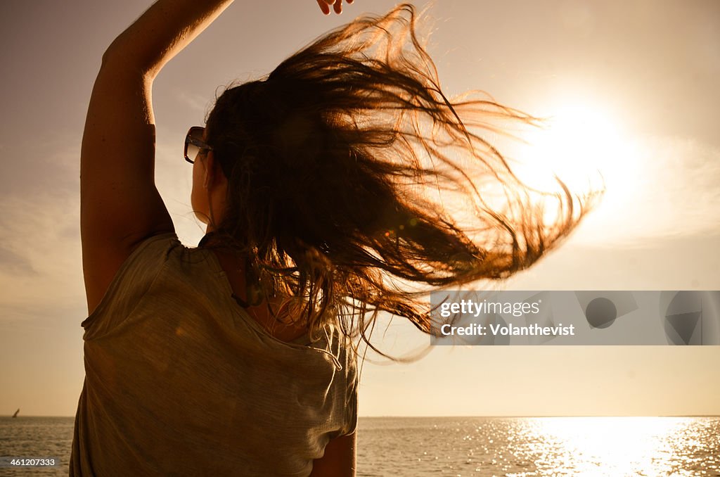 Girl looking the sea w/ hair in the wind at sunset