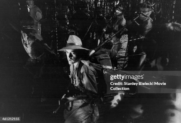 Actor Powers Boothe surrounded by tribesmen with spears, in a scene from the movie 'The Emerald Forest', 1985.