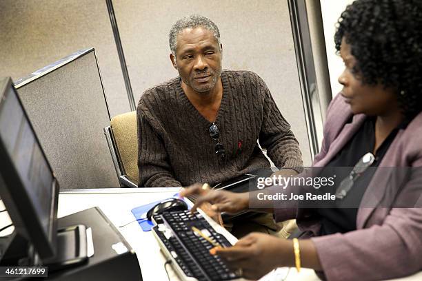 Magny Laguerre sits with career specialists, Sidalouise Charlotin, as she helps him fill out a form for unemployment benefits at a Workforce One...