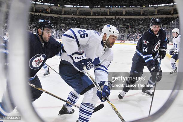Daniel Winnik of the Toronto Maple Leafs plays the puck along the boards as Grant Clitsome and Anthony Peluso of the Winnipeg Jets defend during...