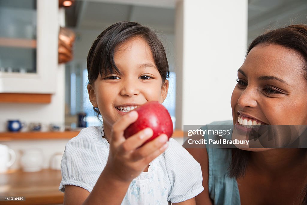 Mother in kitchen with daughter holding red apple