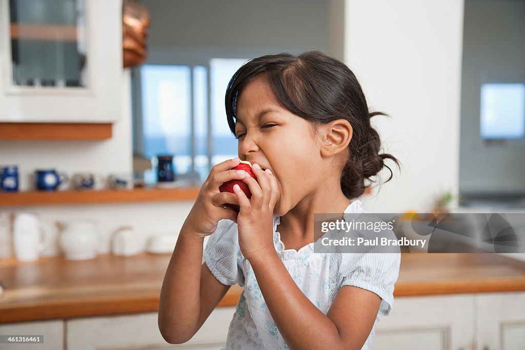 Girl in kitchen eating red apple
