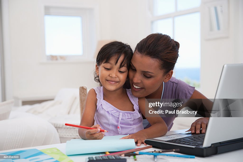 Mother at laptop with daughter drawing