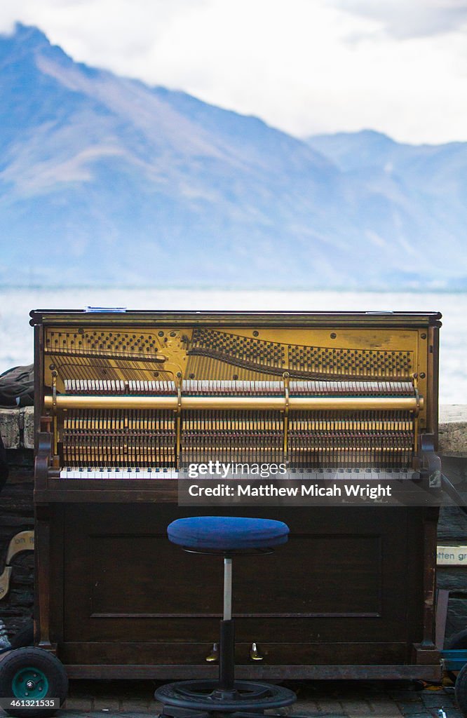 A piano sits lakeside next to mountains