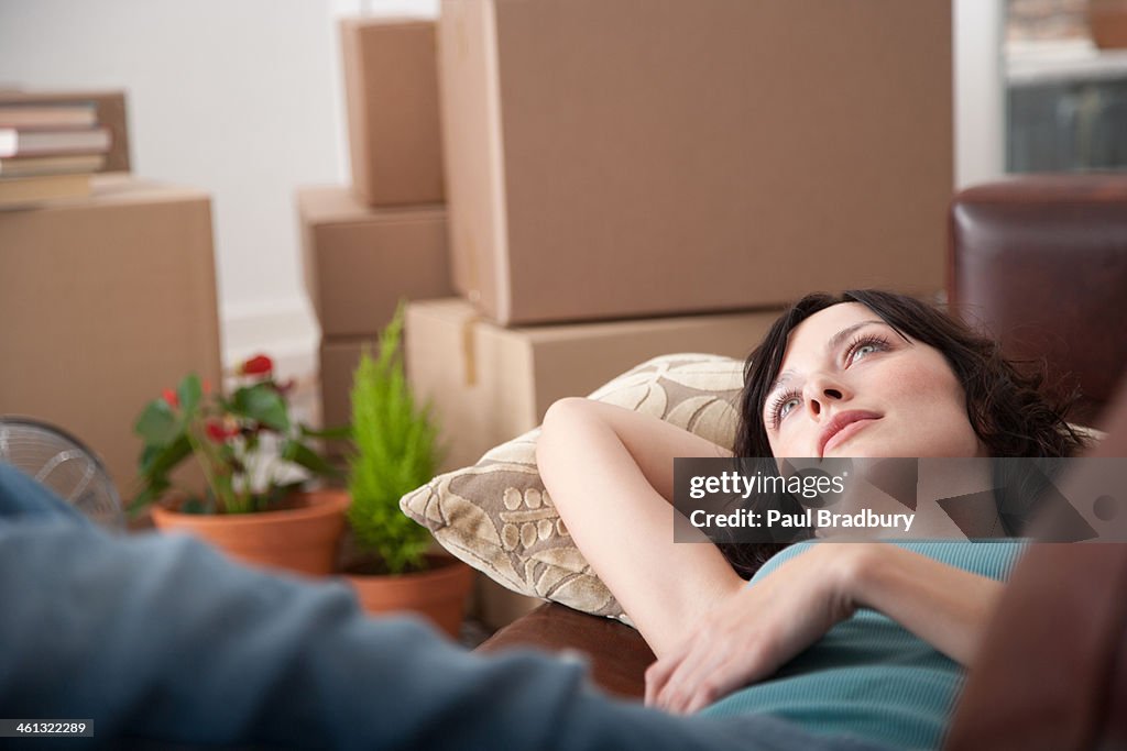 Woman lying down on sofa in home with cardboard boxes