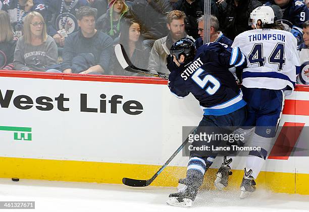 Mark Stuart of the Winnipeg Jets checks Nate Thompson of the Tampa Bay Lightning into the boards as the puck slides down the ice during second period...