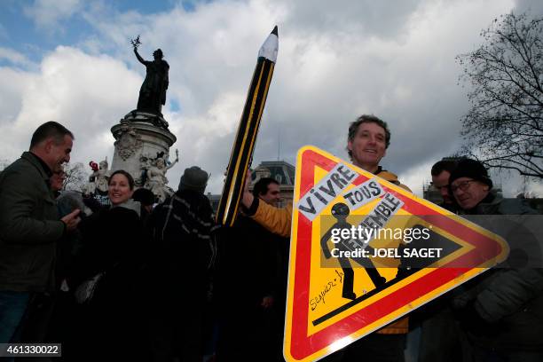 Man holds a replica pencil and a sign that reads, "All live together" at the Place de la Republique at the start of a Unity rally "Marche...