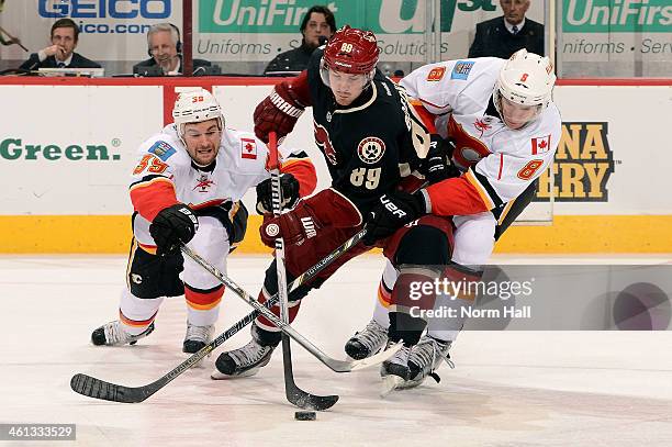 Mikkel Boedker of the Phoenix Coyotes skates the puck between T.J. Galiardi and Joe Colborne of the Calgary Flames during the third period at...