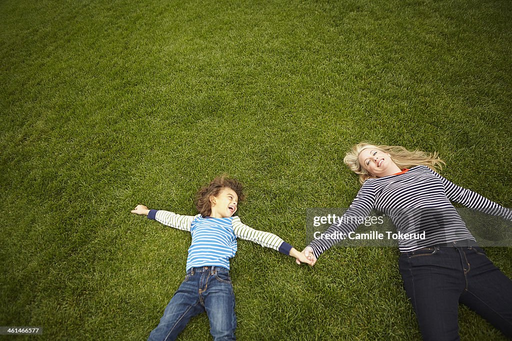 Mother and son holding hands and laying on grass