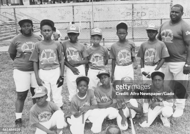 African American youth, coaches and community members gather for a little league game with racist grafitti in the background, Harlem Park, Baltimore,...