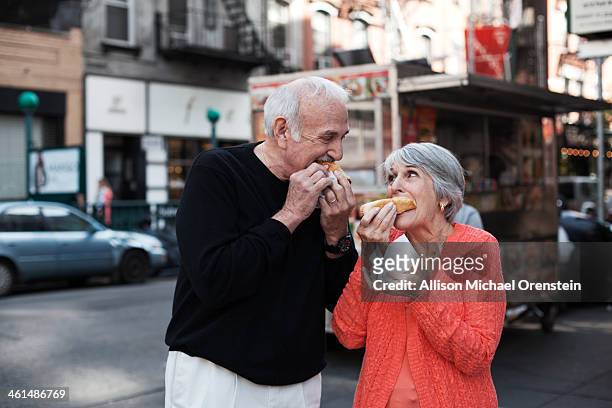 senior couple enjoying hot dogs on city street - new york food stockfoto's en -beelden
