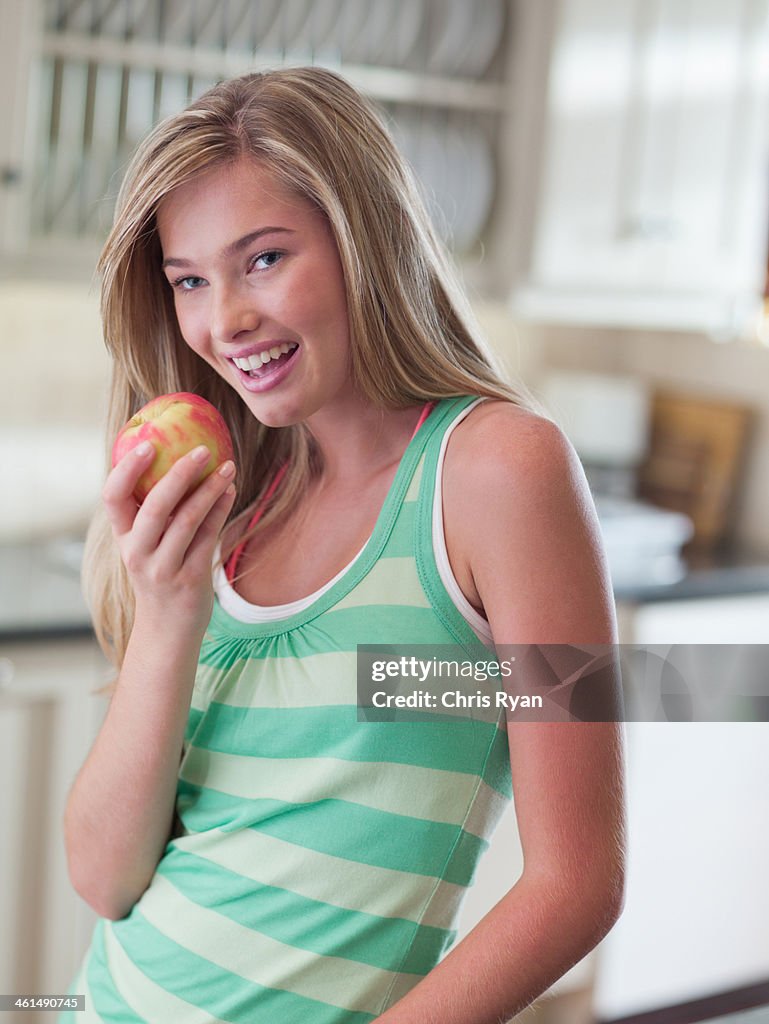 Teenage girl in kitchen eating an apple